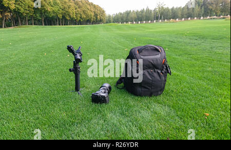 A camera, bag and gimbal sitting on lush grass in a city park. Stock Photo