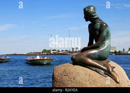 Copenhagen, Denmark - June 27, 2018: The Little Mermaid bronze statue by Edvard Eriksen, with sightseeing boats in the background. Stock Photo