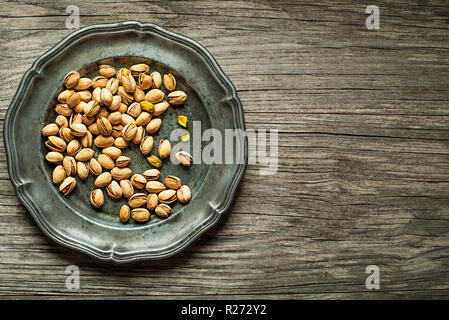 Roasted Pistachios nuts in plate on wooden table background Stock Photo