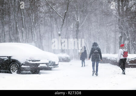 People walking through city street covered with snow during heavy snowfall. Blizzard in town at winter. Natural disasters, snow storm Stock Photo