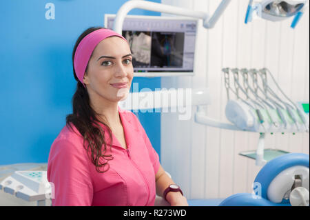 Beautiful young woman assistant at chair in dentist studio, looking at camera, model released Stock Photo
