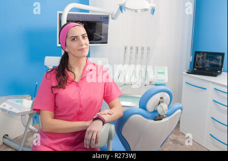 Beautiful young woman assistant at chair in dentist studio, looking at camera, model released Stock Photo