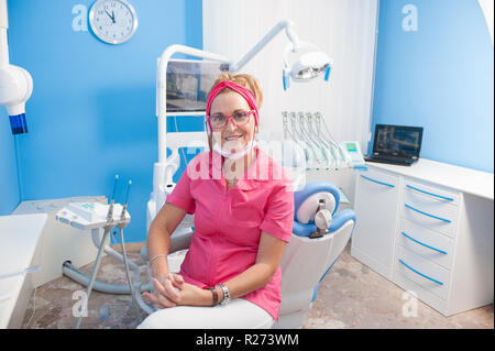 Beautiful aged woman assistant at chair in dentist studio, smiling looking at camera, model released Stock Photo
