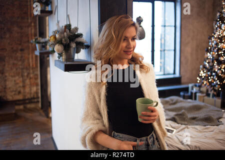 First day of the new year. Happy and confident young woman at home drinking morning coffee. the background of an apartment with a decorated Christmas  Stock Photo