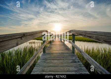 coastal waters with a very long wooden boardwalk pier in the center during a colorful summer sunset under an expressive sky with reflections in waterP Stock Photo