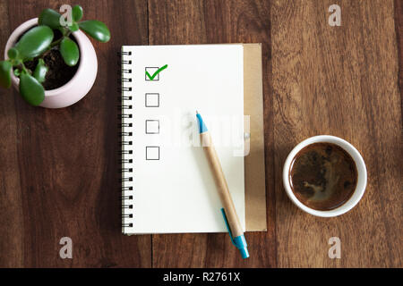 tick box in notepad on table. top view of wooden table with blank notepad, pen and cup of coffee. Stock Photo