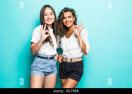 Mixed race women colleagues make okay gesture, confirm they can handle work, dressed in casual clothes, pose against blue background. Multiracial girl Stock Photo