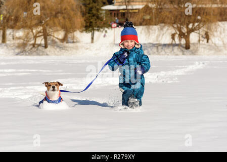 Happy kid with dog on leash playing on intact fresh snow at sunny winter day Stock Photo