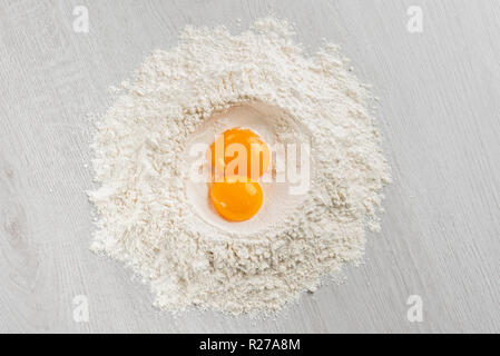 pile of flour with egg yolks for dough on table, top view. Stock Photo