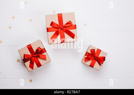 Three present boxes with red bow on white wooden background with golden confetti. Flat lay, place for text. Stock Photo