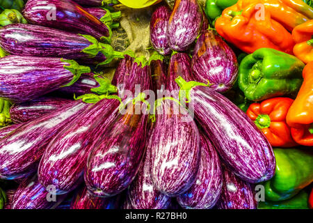 Vibrant purple striped eggplants and fresh bell peppers displayed at a traditional farmers market in Valencia Stock Photo
