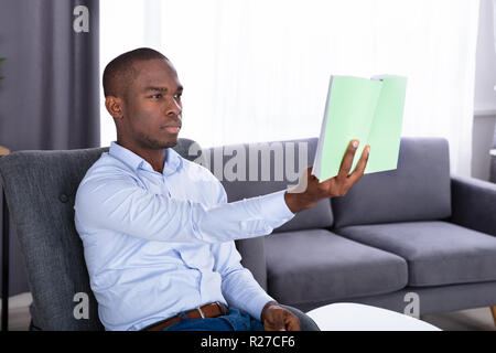Young African Man Sitting On Chair Holding Book At Home Stock Photo