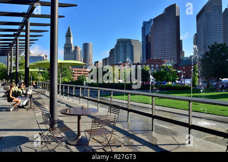 Open plaza on Rose Kennedy Greenway with tables and chairs and tall buildings of Boston financial district behind Stock Photo