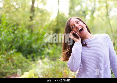 Young brunette girl talking on mobile phone laughing very happily in a very green forest Stock Photo