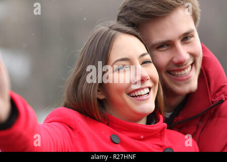 Portrait of a happy couple in red with perfect smile taking selfies outdoors in winter Stock Photo