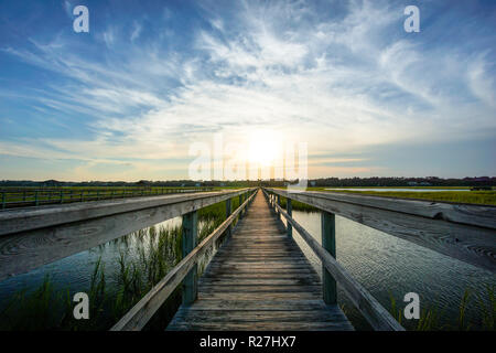 coastal waters with a very long wooden boardwalk pier in the center during a colorful summer sunset under an expressive sky with reflections in waterP Stock Photo