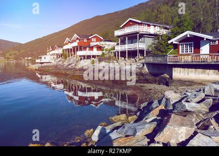 rorbuer - traditional norwegian red wooden house to stand at the lakeside and mountains in the distance, norway Stock Photo