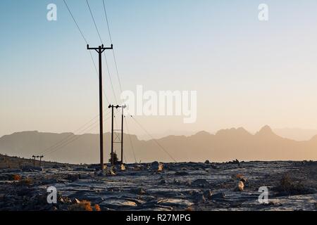 Pylons with power lines in mountains at colorful sunset, Oman Stock Photo