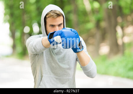 Man in boxing gloves and hood on natural landscape. Boxer exercise on fresh air. Knowckout. Man punching. Fight for success. Training his boxing skills. Born to fight. Power and energy. Stock Photo