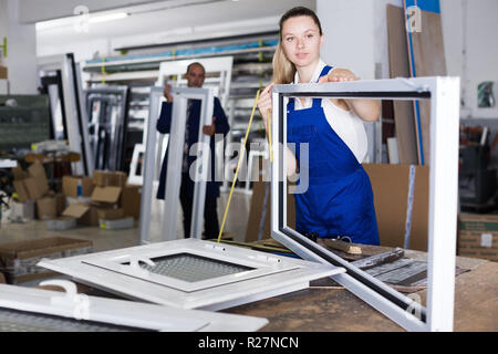 Female worker manufacturing plastic windows using measuring tape at workshop Stock Photo