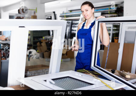 Diligent  positive  workwoman assembling PVC window in workshop with manual tools Stock Photo