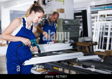 Portrait of young workwoman using electric drill on plastic window frame at factory Stock Photo