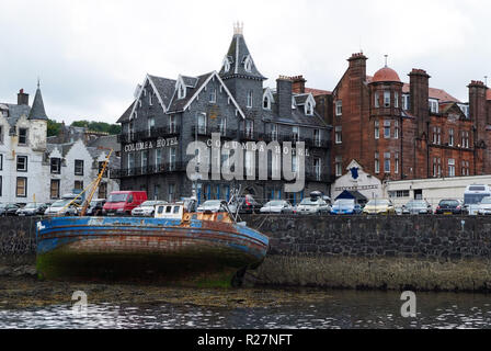 Oban, United Kingdom - February 20, 2010: shipwreck and city architecture along sea quay. Bay with houses on grey sky. Resort town with hotels. Summer vacation on island. Travelling and wanderlust. Stock Photo