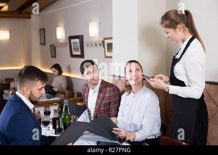 Positive waitress taking order from visitors, using digital tablet Stock Photo