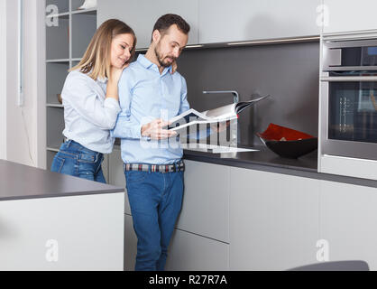 Young loving couple standing with book in kitchen, designing new interior Stock Photo