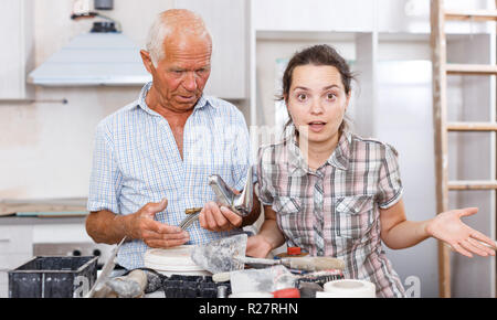 Young woman and her elderly father discussing installing faucet during repairs in their apartment Stock Photo