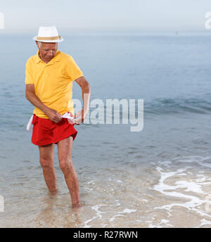 Serious mature man in headwear shows empty pockets near ocean Stock Photo
