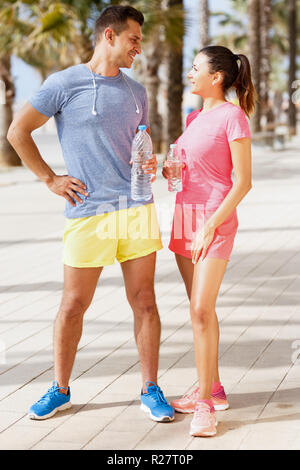 Lifestyle portrait of young sporty couple drinking water and relaxing after outdoor workout Stock Photo