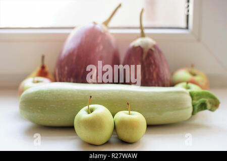 Whole ripe squash, apples, aubergines lie on the windowsill. Stock Photo