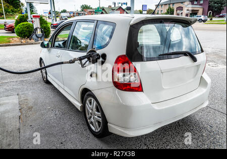 Horizontal angled shot from the rear toward the front of a generic small white car being filled with gasoline. Stock Photo