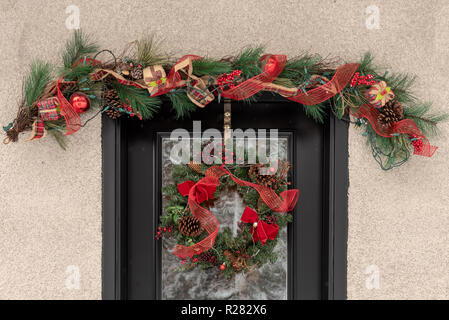 Traditional Christmas wreath hung on door with snowy background reflection Stock Photo