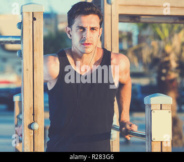 Happy  positive  strong man doing parallel bar dips to music on sports ground on beach Stock Photo