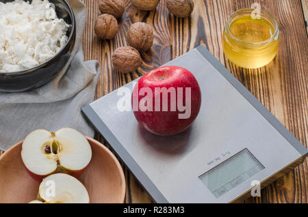 Healthy food. A red apple lies on a metal scale on a wooden table, next to it is a plate with cottage cheese, a plate with a cut apple, nuts lie and a Stock Photo