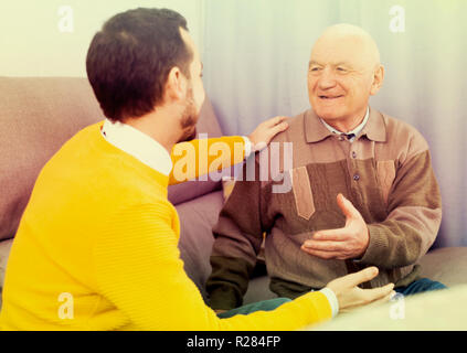 Aged father and his young son warmly communicate at home on couch Stock Photo