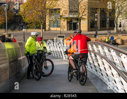 Newcastle, England, United Kingdom, 17th November 2018. Cyclists stop for a chat on the Gateshead Millennium Bridge over the River Tyne with pedestrians on The Quayside Stock Photo