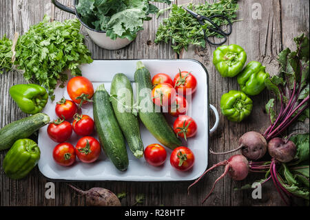 Freshly picked heirloom tomatoes, zucchini, beets, kale, peppers, cilantro and oregano on an old barn wood background. Stock Photo
