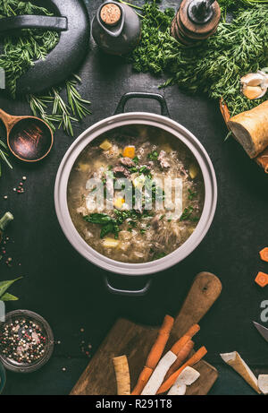 Healthy low carb beef and cabbage soup or stew in cast iron cooking pot on dark background with ingredients and wooden spoon, top view. Healthy clean  Stock Photo