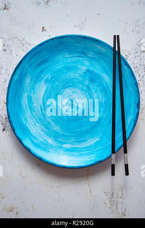 Turquoise hand painted ceramic serving plate with wooden chopsticks on side Stock Photo