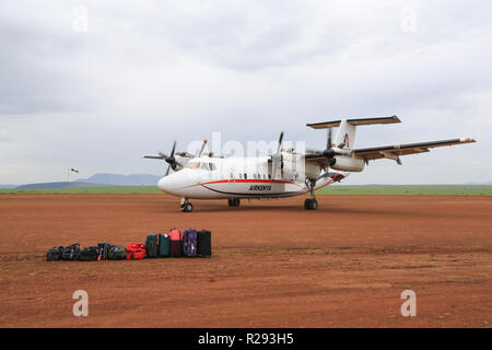 An Airkenya plane is taxiing toward waiting passengers and their luggage at the Keekorok Airstrip in Masai Mara National Reserve, Narok County, Kenya. Stock Photo