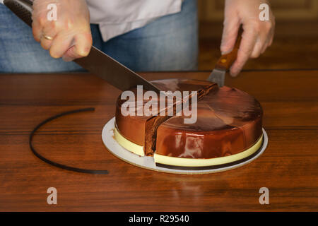 Prague mousse cake. Woman cuts off piece of cake with a kitchen knife. Mirror glaze glitters deliciously. Modern cooking. Cooking in a pastry shop. Stock Photo