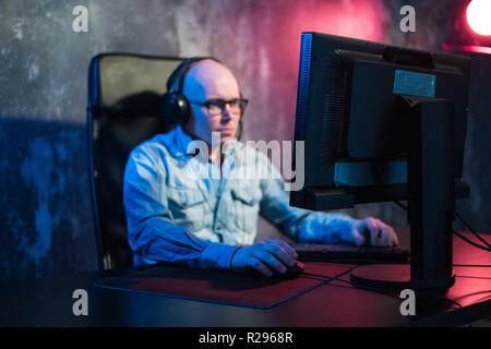 Favorite hobby. Selective profile of concentrated young gamer in headphones is sitting in computer club. Playing virtual reality video game. Stock Photo