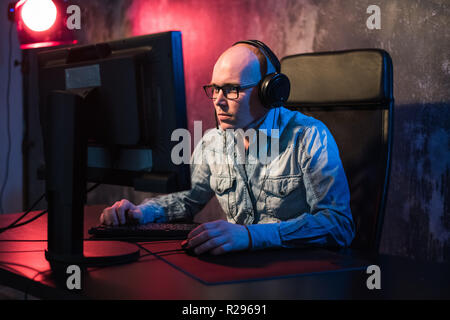 Favorite hobby. Selective profile of concentrated young gamer in headphones is sitting in computer club. Playing virtual reality video game. Stock Photo