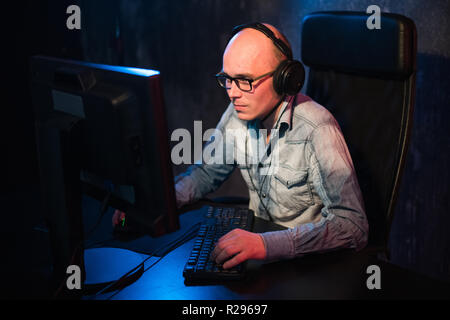 Serious young man sitting and working with computer in dark office. Stock Photo