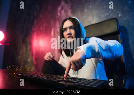 Woman in the hood sitting and working at laptop as hacker. Running malware program on computer in the internet with malevolent smile on her face Stock Photo