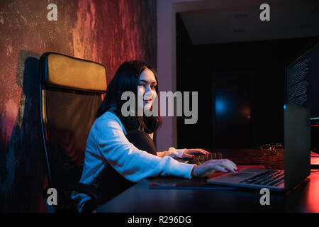 Young woman sit in front of personal computer and laptop, php Programming Html Coding Cyberspace Concept. Looking at camera. Stock Photo