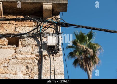 Electric wires attached on an old stone house. Old architecture. Electricity transmission. Light bulb on the building. Street light. Stock Photo